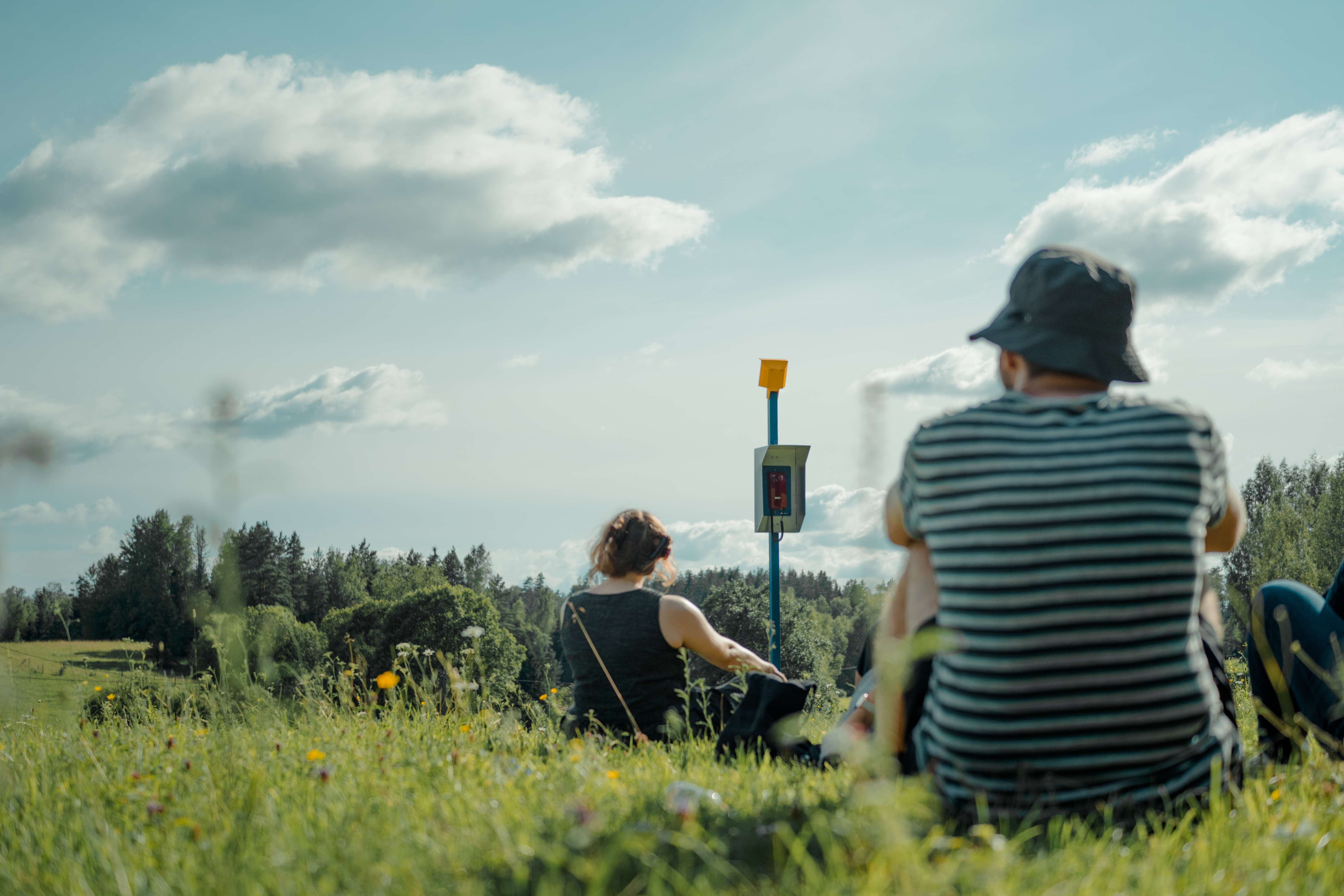 Visitors sitting with a Nephophile, facing the same open sky. Maajaam, Estonia, July 2025. Photo by Ya Chuan Chen